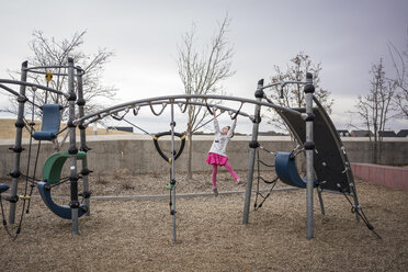 Mädchen hängt auf dem Spielplatz an einem Klettergerüst bei bewölktem Himmel - CAVF53896