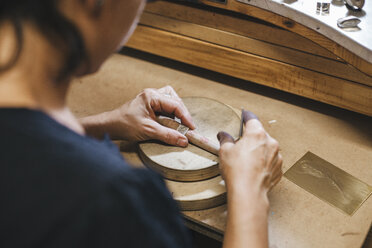Hochformatige Ansicht eines weiblichen Handwerkers, der einen Ring auf einem Holztisch in einer Werkstatt misst - CAVF53903
