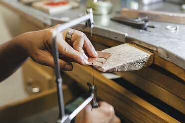 Abgeschnittene Hände einer Handwerkerin, die eine Handsäge benutzt, während sie an einem Tisch in einer Werkstatt arbeitet - CAVF53911