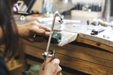 Abgeschnittene Hände eines weiblichen Handwerkers, der mit einer Handsäge auf einem Tisch in einer Werkstatt Geräte schneidet - CAVF53916