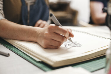 Midsection of female artist drawing on book in workshop - CAVF53920