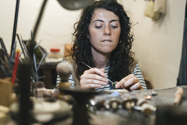 Mittelteil einer Kunsthandwerkerin, die einen Ring herstellt, während sie am Tisch in der Werkstatt sitzt - CAVF53924