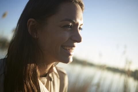 Nahaufnahme einer lächelnden jungen Frau, die bei Sonnenuntergang in den Himmel schaut, lizenzfreies Stockfoto