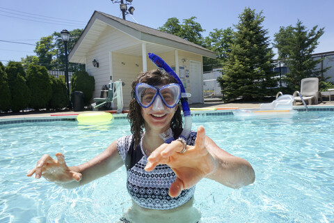 Porträt einer glücklichen Frau, die einen Schnorchel trägt, während sie an einem sonnigen Tag im Pool schwimmt, lizenzfreies Stockfoto