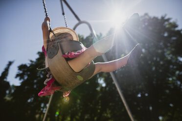 Low angle view of playful girl swinging on swing at playground during sunny day - CAVF53959