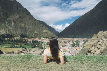 Rückansicht eines weiblichen männlichen Wanderers, der auf einem Berg sitzend das Dorf gegen den Himmel in Pisac betrachtet - CAVF53987