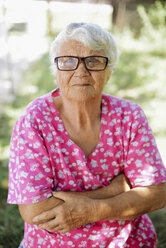 Porträt einer älteren Frau mit verschränkten Armen und Brille im Hinterhof - CAVF53997