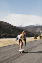 Full length of carefree young woman skateboarding on road during sunny day - CAVF54029