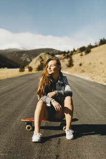 Unbeschwerte junge Frau in voller Länge auf dem Skateboard sitzend an einem sonnigen Tag - CAVF54031