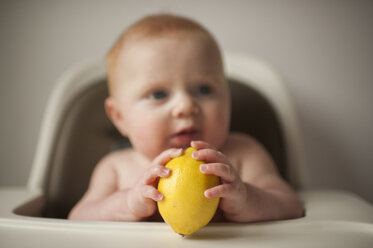 Shirtless Baby Junge hält Zitrone, während auf Hochstuhl zu Hause sitzen - CAVF54040