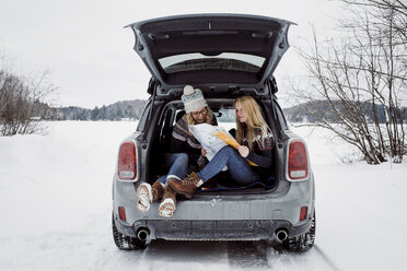 Glückliche Freundinnen lesen eine Karte, während sie im Winter im Kofferraum eines Autos sitzen - CAVF54070
