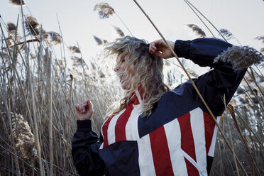 Fröhliche Frau in Jacke mit amerikanischer Flagge tanzt inmitten von Pflanzen auf einem Feld - CAVF54074