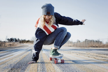 Volle Länge der spielerischen Frau Skateboarding auf der Straße im Winter - CAVF54076