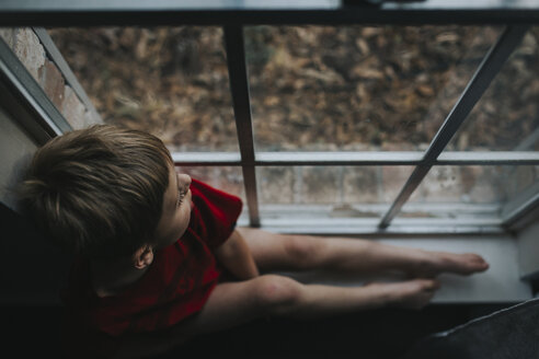 Hoher Blickwinkel des nachdenklichen Jungen, der durch das Fenster zu Hause schaut - CAVF54079