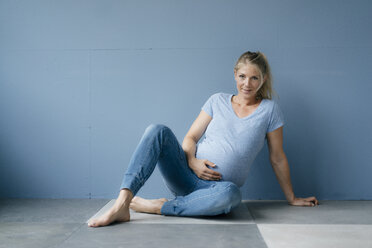 Portrait of smiling pregnant woman sitting on the floor - KNSF05202