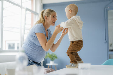 Happy pregnant mother with toddler son standing on table - KNSF05203