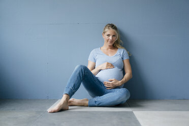 Porträt einer lächelnden schwangeren Frau, die auf dem Boden sitzt - KNSF05204