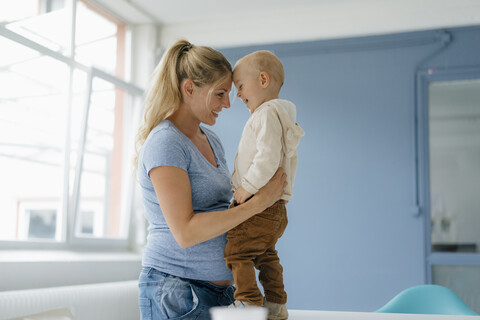 Glückliche schwangere Mutter umarmt Kleinkind Sohn stehen auf dem Tisch, lizenzfreies Stockfoto