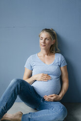 Portrait of smiling pregnant woman sitting on the floor with closed eyes - KNSF05210