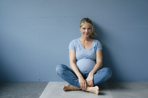 Portrait of smiling pregnant woman sitting on the floor - KNSF05213