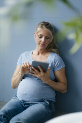 Schwangere Frau auf dem Boden sitzend mit Tablet - KNSF05216
