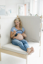 Smiling pregnant woman holding headphones at her belly - KNSF05229