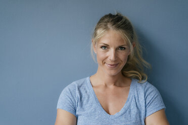 Portrait of smiling blond woman standing at blue wall - KNSF05230