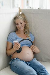 Smiling pregnant woman holding headphones at her belly - KNSF05231