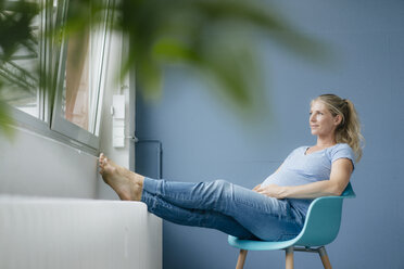 Schwangere Frau sitzt auf einem Stuhl am Fenster - KNSF05239