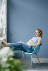 Schwangere Frau sitzt auf einem Stuhl am Fenster - KNSF05241