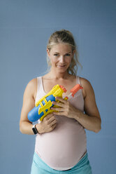 Portrait of smiling pregnant woman holding water gun - KNSF05255