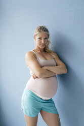 Portrait of confident pregnant woman standing at blue wall - KNSF05261