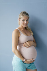 Portrait of smiling pregnant woman standing at blue wall - KNSF05263