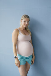 Portrait of smiling pregnant woman standing at blue wall - KNSF05266