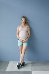 Portrait of smiling pregnant woman standing at blue wall - KNSF05267