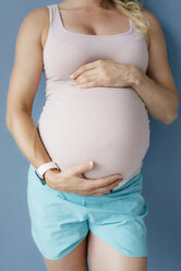 Mittelteil einer schwangeren Frau, die an einer blauen Wand steht - KNSF05269