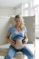 Pregnant woman holding headphones at her belly - KNSF05276