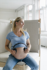 Pregnant woman holding headphones at her belly - KNSF05277
