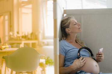 Pregnant woman holding headphones at her belly - KNSF05278