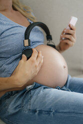 Mid-section of pregnant woman holding headphones at her belly - KNSF05279