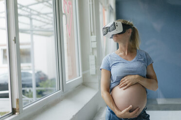 Pregnant woman wearing VR glasses at the window - KNSF05283
