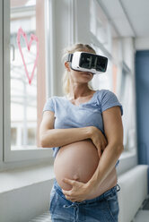 Pregnant woman wearing VR glasses at the window - KNSF05284