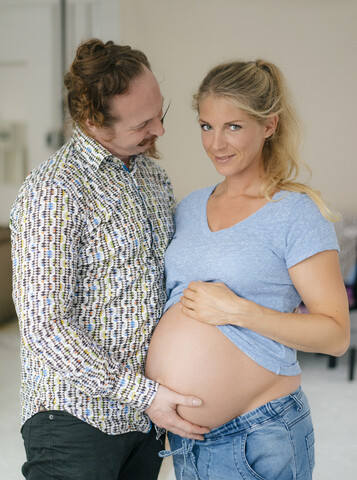 Mann berührt den Bauch einer lächelnden schwangeren Frau, lizenzfreies Stockfoto