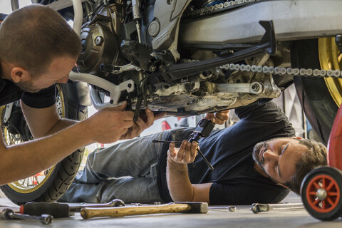 Mechaniker, der in der Werkstatt an einem Motorrad arbeitet, gefilmt von seinem Partner, lizenzfreies Stockfoto