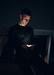 Sportive young man with smartphone and earphones outdoors at night - ZEDF01735