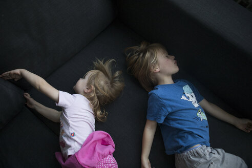 Bruder und Schwester liegen Rücken an Rücken auf der Couch - JLOF00296