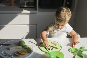 Kleiner Junge sitzt am Tisch in der Küche und isst Obst - MOMF00533