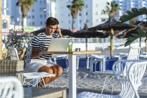 Mann mit Laptop auf der Terrasse einer Strandbar, lizenzfreies Stockfoto