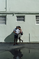 Smiling young couple standing at building at a puddle - BOYF00789