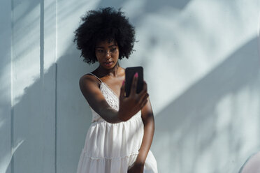 Young woman wearing white dress taking a selfie at a wall - BOYF00814